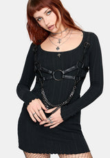 Woman wearing a black ribbed dress with a black harness and chain details on a white background