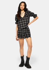 Woman wearing a black and gray plaid shorts and matching top with boots on a white background