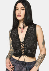 Woman wearing a black lace-up top with intricate designs on a plain background