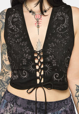 Woman wearing a black lace-up top with intricate designs on a plain background