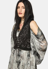 Woman wearing a black embroidered top over a long, flowing dress with abstract patterns on a white background