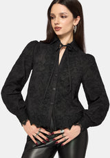 Woman wearing a black long sleeve lace detail blouse with a plain background