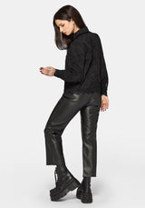 Woman wearing a black long sleeve blouse with leather pants on a white background