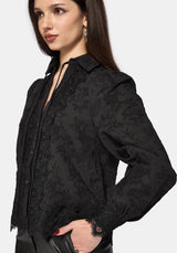Woman wearing a black long sleeve lace detail blouse with a plain background