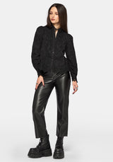Woman wearing a black long sleeve lace detail blouse with black leather pants on a plain background