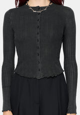 A woman wearing a dark charcoal gray ribbed long-sleeve cardigan with a button-front detail and scalloped hem, styled with a chunky silver chain necklace against a light gray background.