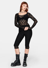 Woman wearing a black long sleeve lace top with black capri pants against a white background