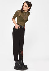 Woman wearing a green top and black pants with floral designs on a white background