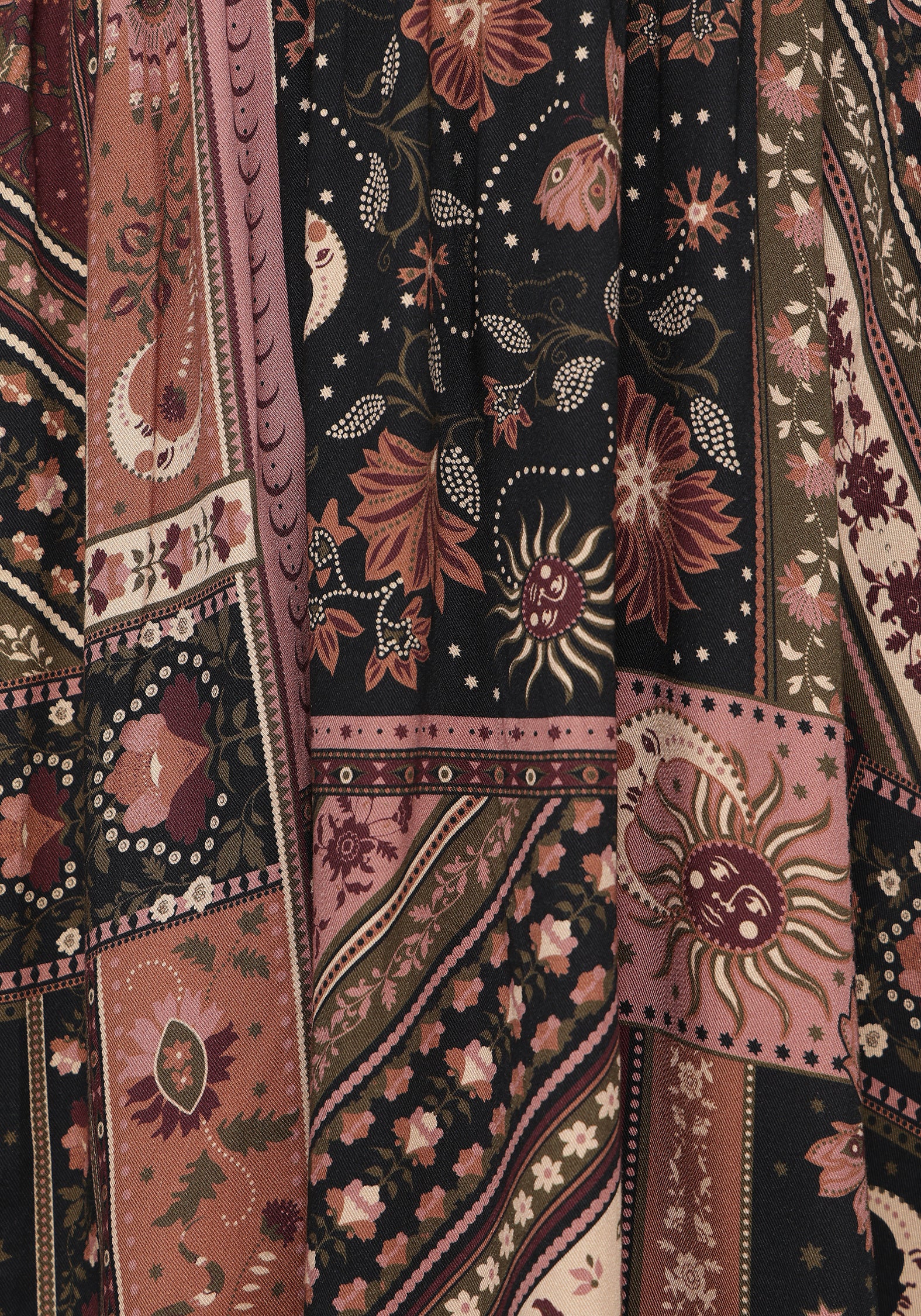 A close-up of a patterned textile with mixed panels in dusty pink, rust red, black, and beige, featuring floral, sunburst, and geometric motifs.