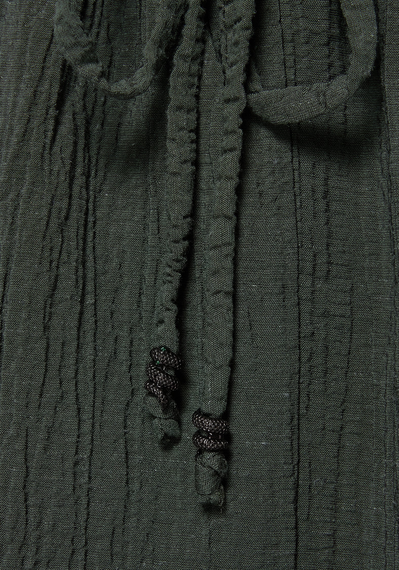 Close-up of a dark olive green crinkled fabric with matching drawstrings and black twisted cord ends.