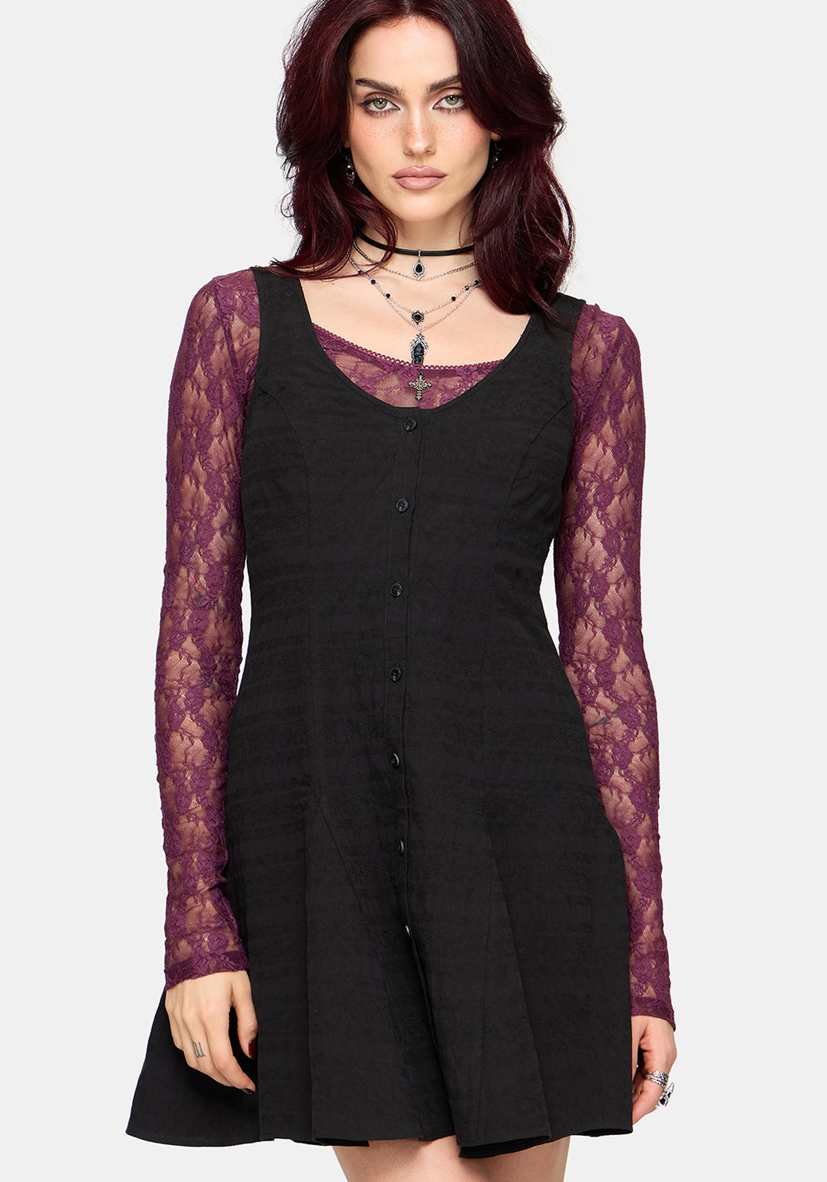 Woman wearing a black mini dress with purple lace long sleeved top underneath on a white background