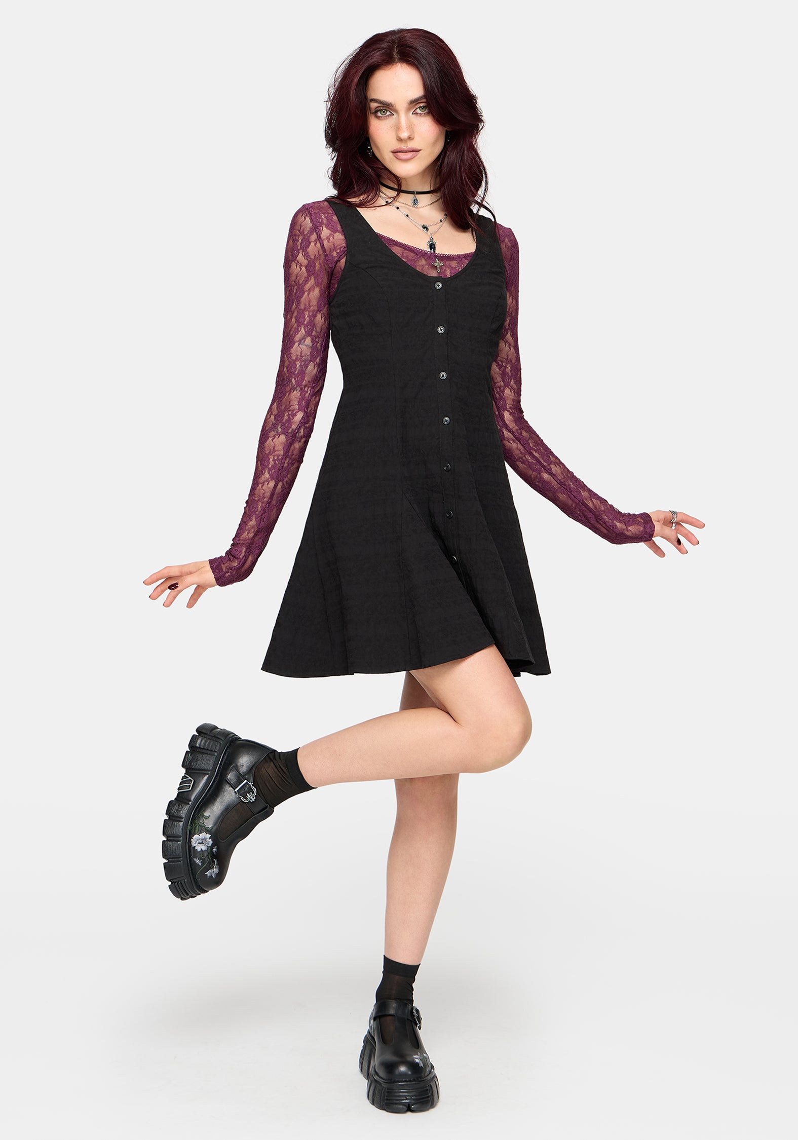 Woman wearing a black dress with a purple long sleeved top underneath, against a white background