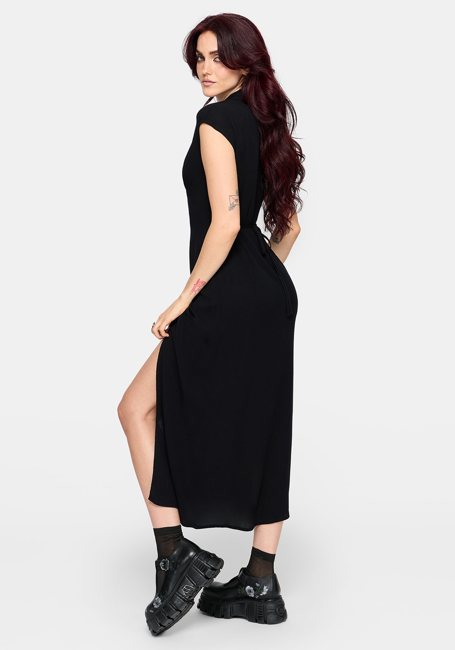 Woman wearing a black midaxi dress with a slit on a white background