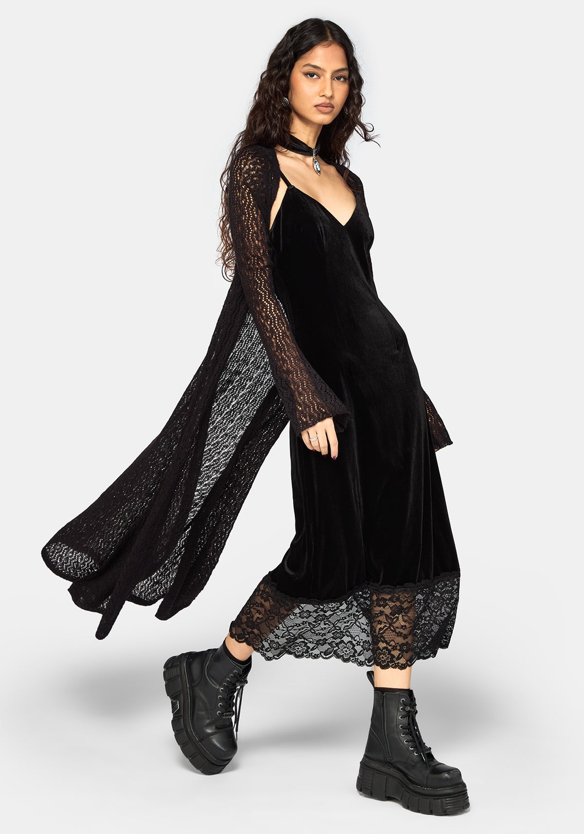A model wearing a black midi cardigan with long sheer sleeves and  styled with black combat boots against a light gray studio background.