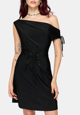 A woman modeling a black one-shoulder mini dress with a side tie detail, holding a black studded shoulder bag against a light gray background.