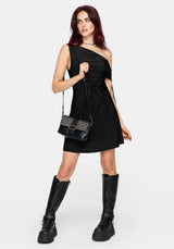 A model wearing a black one-shoulder mini dress with a high-waisted corset-style waist, black knee-high platform boots, and a black studded shoulder bag, posed against a light gray studio background.