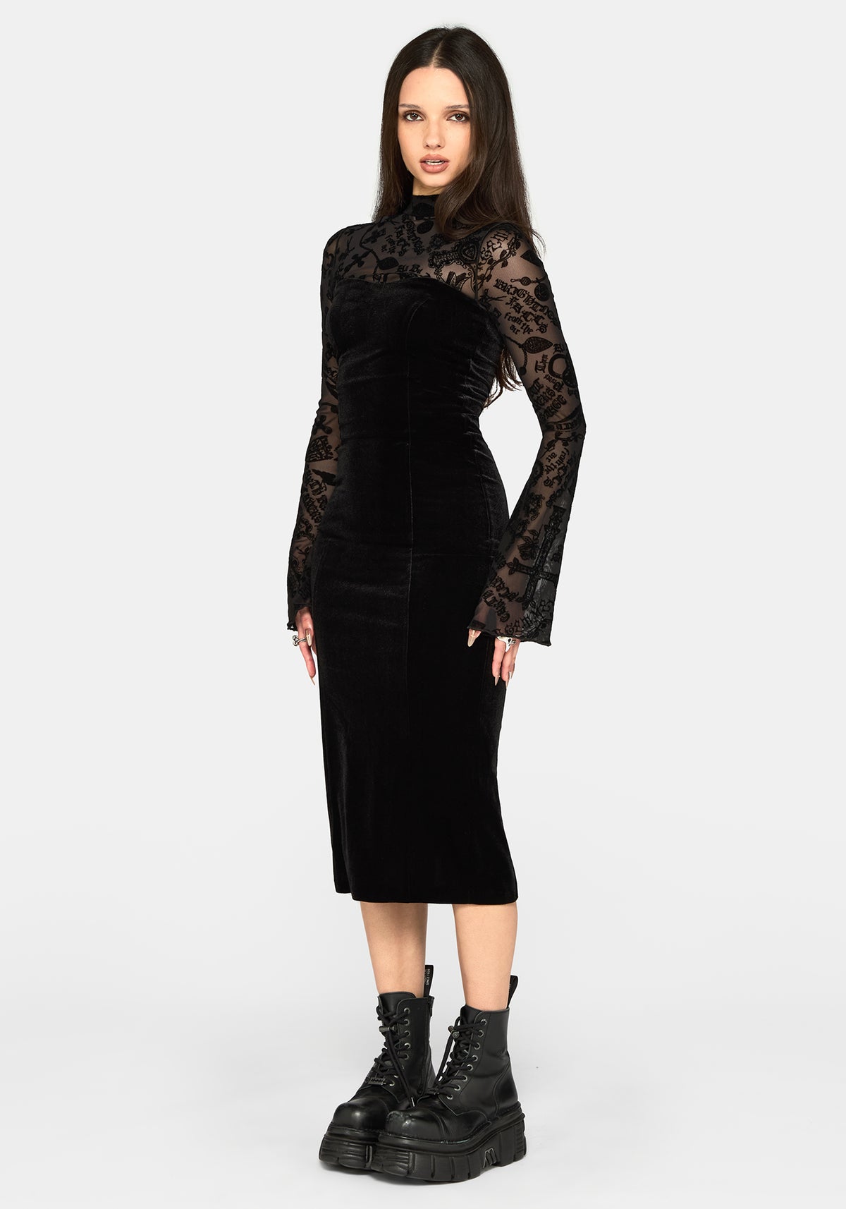 A model wearing a black velvet midi dress with sheer black lace long sleeves and high neck, paired with black combat boots, against a light gray studio background.