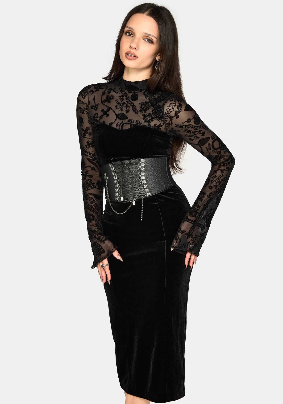 A woman modeling a black gothic-style dress featuring a sheer floral lace long-sleeve top half, a black velvet midriff, a wide black corset-style waist belt with silver studs and chains, and a black velvet pencil skirt bottom half, set against a solid light gray background.