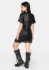 A woman shown from the back wearing a black satin-like short dress with lace trim at the hem and sleeves, paired with tall black lace-up boots, against a light gray studio background.