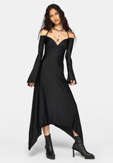 A woman modeling a black off-the-shoulder midi dress with long flared sleeves, a deep V-neckline, and an asymmetrical high-low hem, paired with black ankle boots against a light gray studio background.