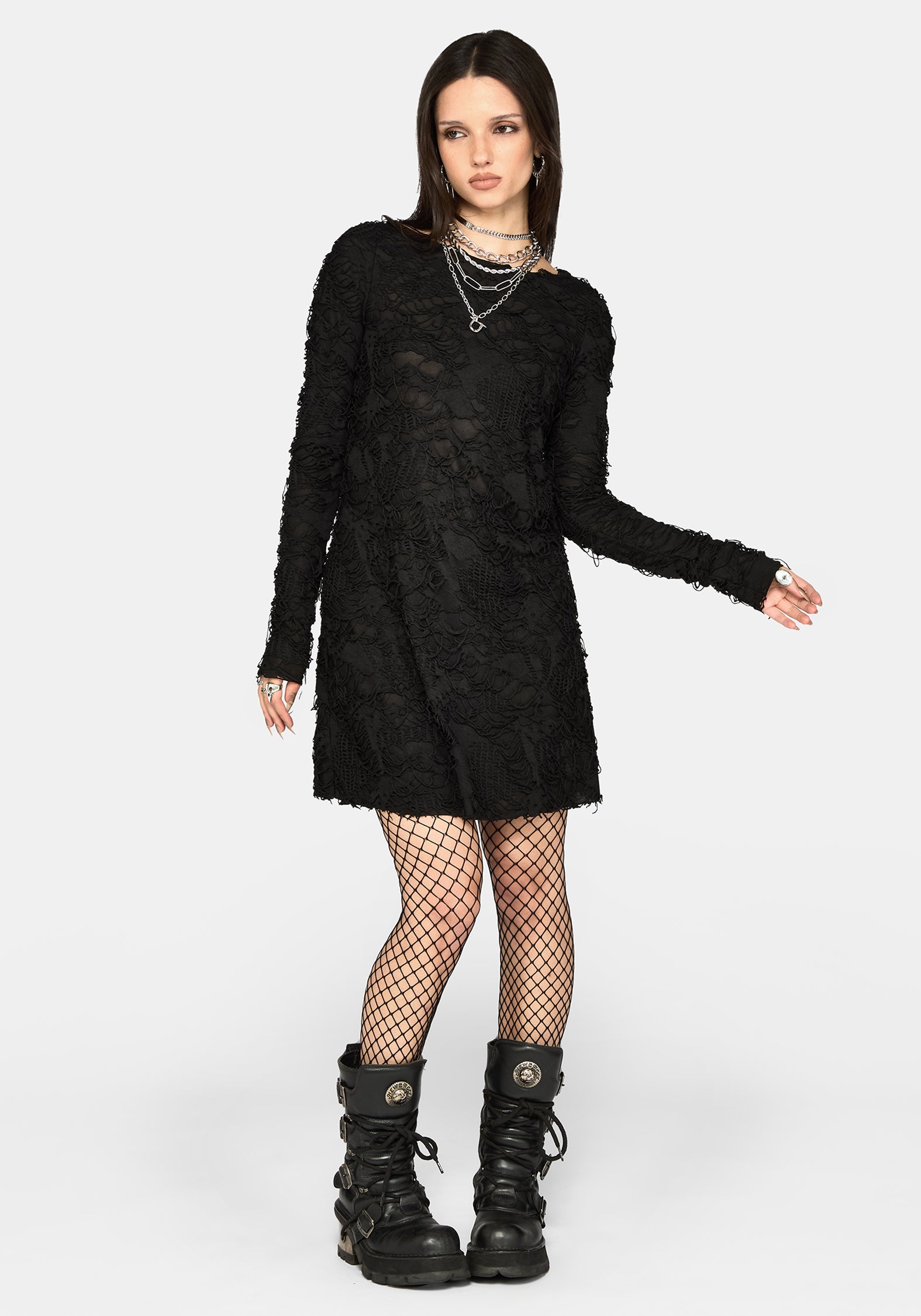 A model wearing a black long-sleeve textured mini dress, black fishnet tights, and black combat boots, standing against a light gray studio background.