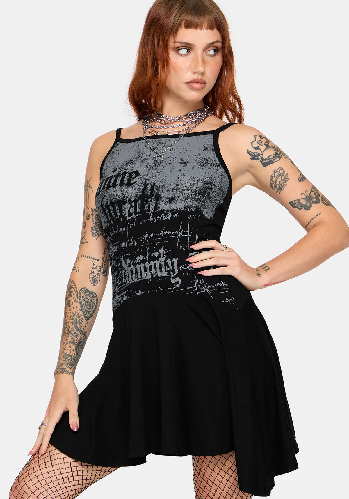 A woman modeling a sleeveless black and gray distressed graphic dress with a flared skirt, paired with fishnet stockings and a choker necklace, against a light gray studio background.