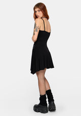A woman modeling a short black spaghetti-strap dress with a flared skirt, paired with black fishnet tights, black cuffed socks, and chunky black platform boots, photographed against a light gray studio background.