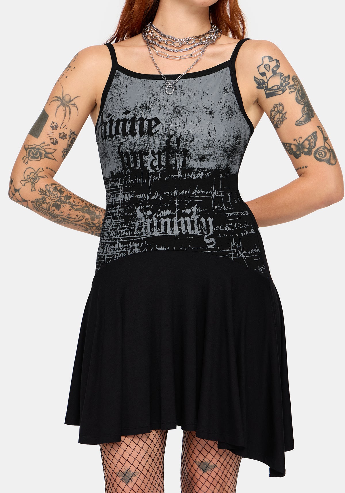 A woman modeling a black and gray distressed graphic mini dress with gothic-style text graphics, shown against a plain light gray background.