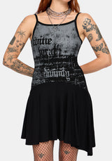 A woman modeling a black and gray distressed graphic mini dress with gothic-style text graphics, shown against a plain light gray background.