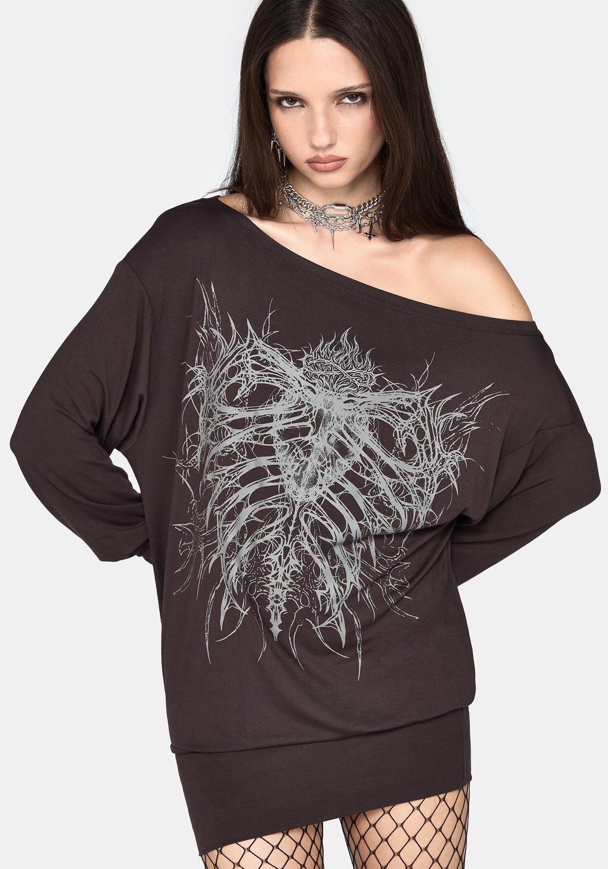 A woman modeling an oversized off-the-shoulder black sweatshirt mini dress with a large white skeleton rib cage graphic on the front, paired with fishnet tights and a silver choker against a light gray background.