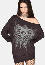 A woman modeling an oversized off-the-shoulder black sweatshirt mini dress with a large white skeleton rib cage graphic on the front, paired with fishnet tights and a silver choker against a light gray background.