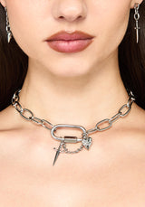 A close-up of a model wearing a chunky silver chain necklace with a large open-link ring, a small chain, and a dangling pointed spike charm.