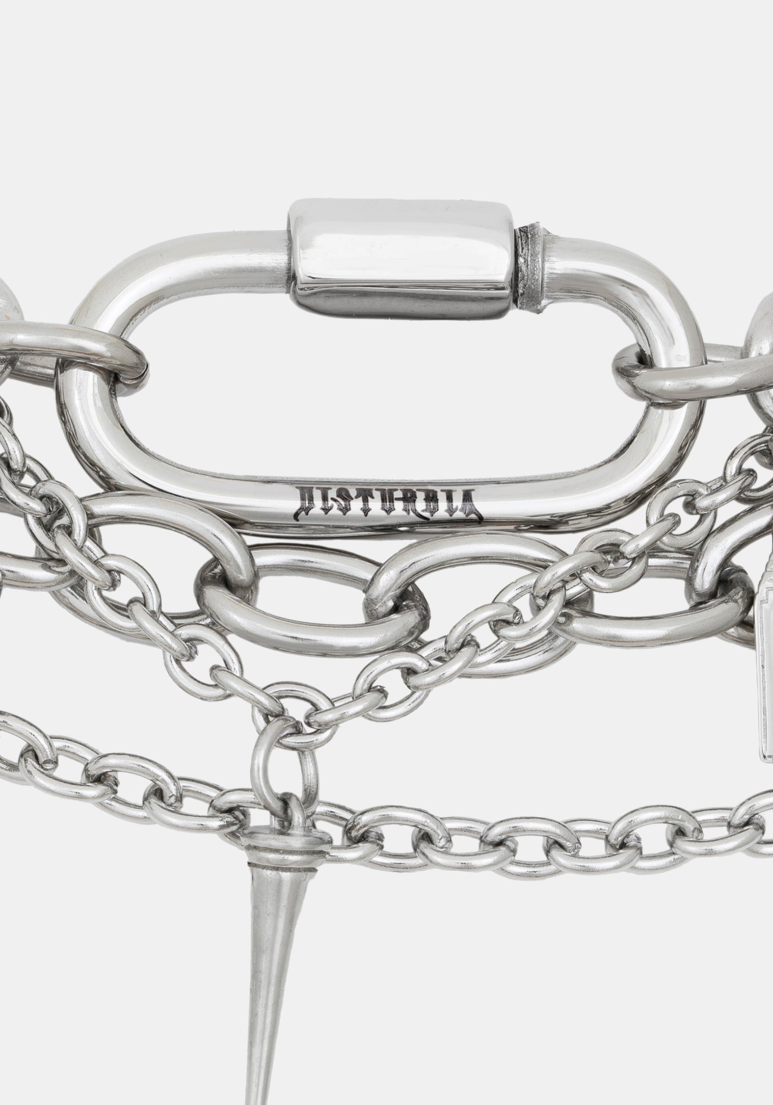 Close-up of a silver-toned chain bracelet featuring a large oval carabiner clasp engraved with 'DISTURBIA', layered chain links, and a pointed spike charm, on a light gray background.