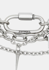 Close-up of a silver-toned chain bracelet featuring a large oval carabiner clasp engraved with 'DISTURBIA', layered chain links, and a pointed spike charm, on a light gray background.