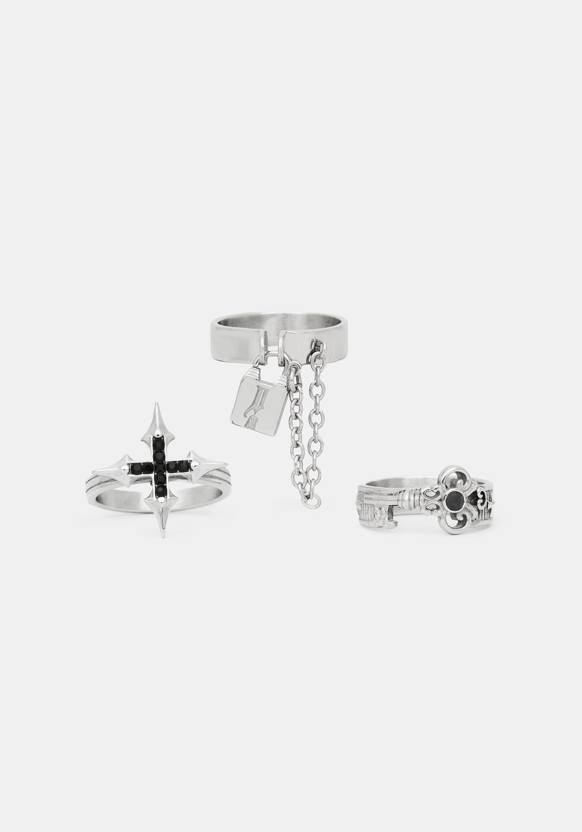 Three silver-toned gothic-style rings displayed on a light gray background, including a cross ring with black accents, a ring with a hanging chain and padlock charm, and a ring with a skull detail.