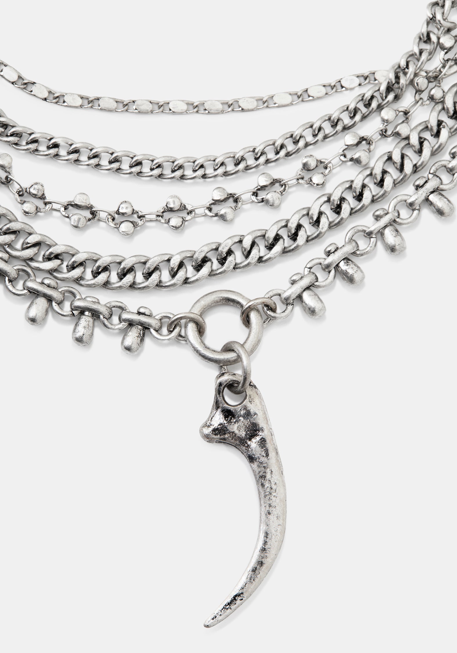 A layered silver-tone chain necklace featuring multiple textured chains, small skull-shaped links, and a curved claw or fang pendant, shown on a light gray background.