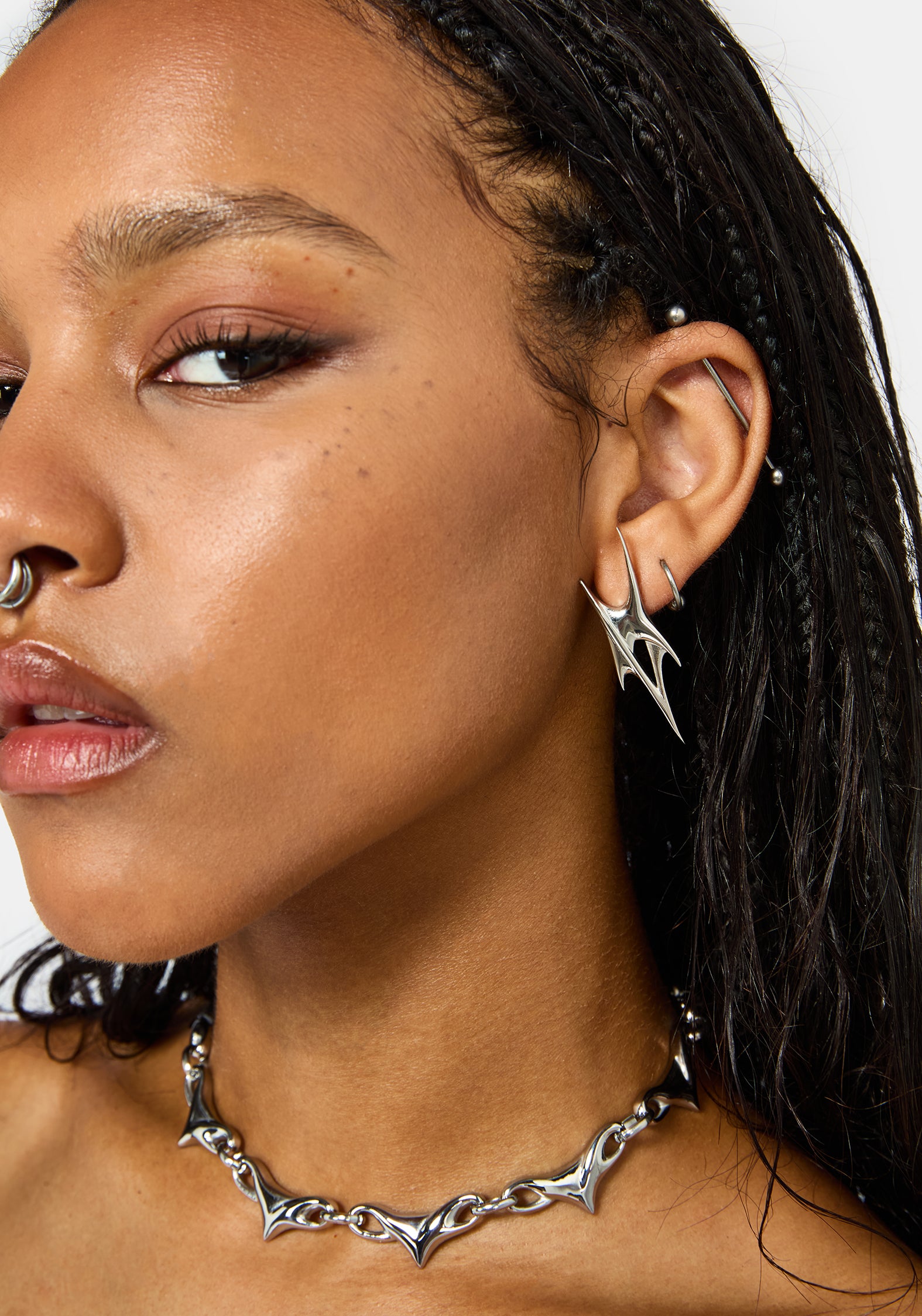 Close-up of a model wearing a silver gothic-style spiked chain necklace and matching spike stud earrings.
