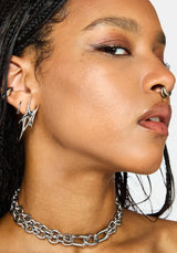 A close-up side profile of a model wearing a chunky silver chain choker necklace, a silver nose ring, and a silver hoop earring with a matching spike drop earring.