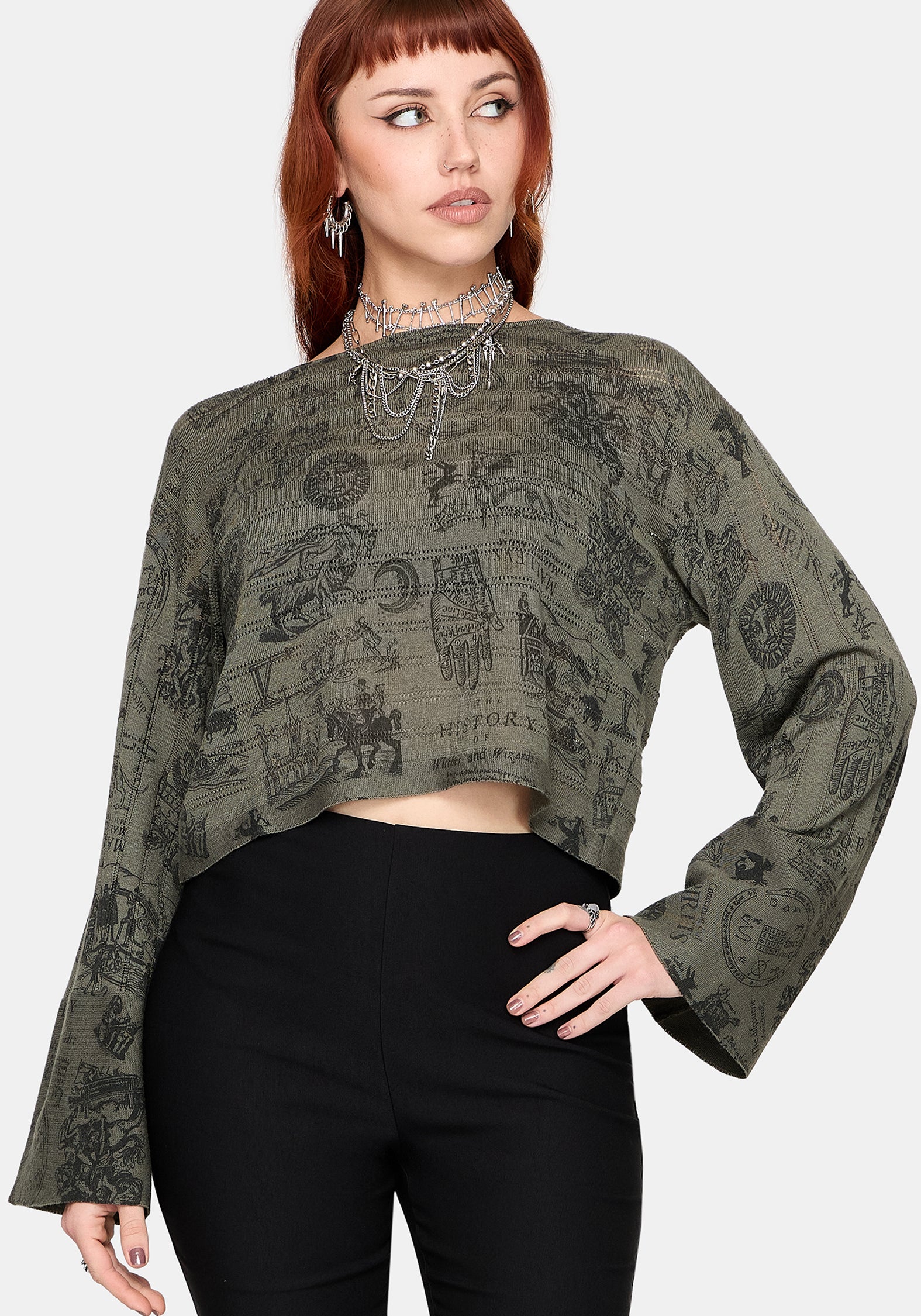 Woman wearing a patterned green jumper and black pants against a plain background