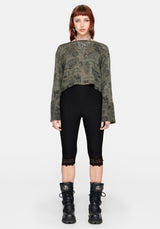 Woman wearing a patterned green jumper and black capri leggings against a plain background