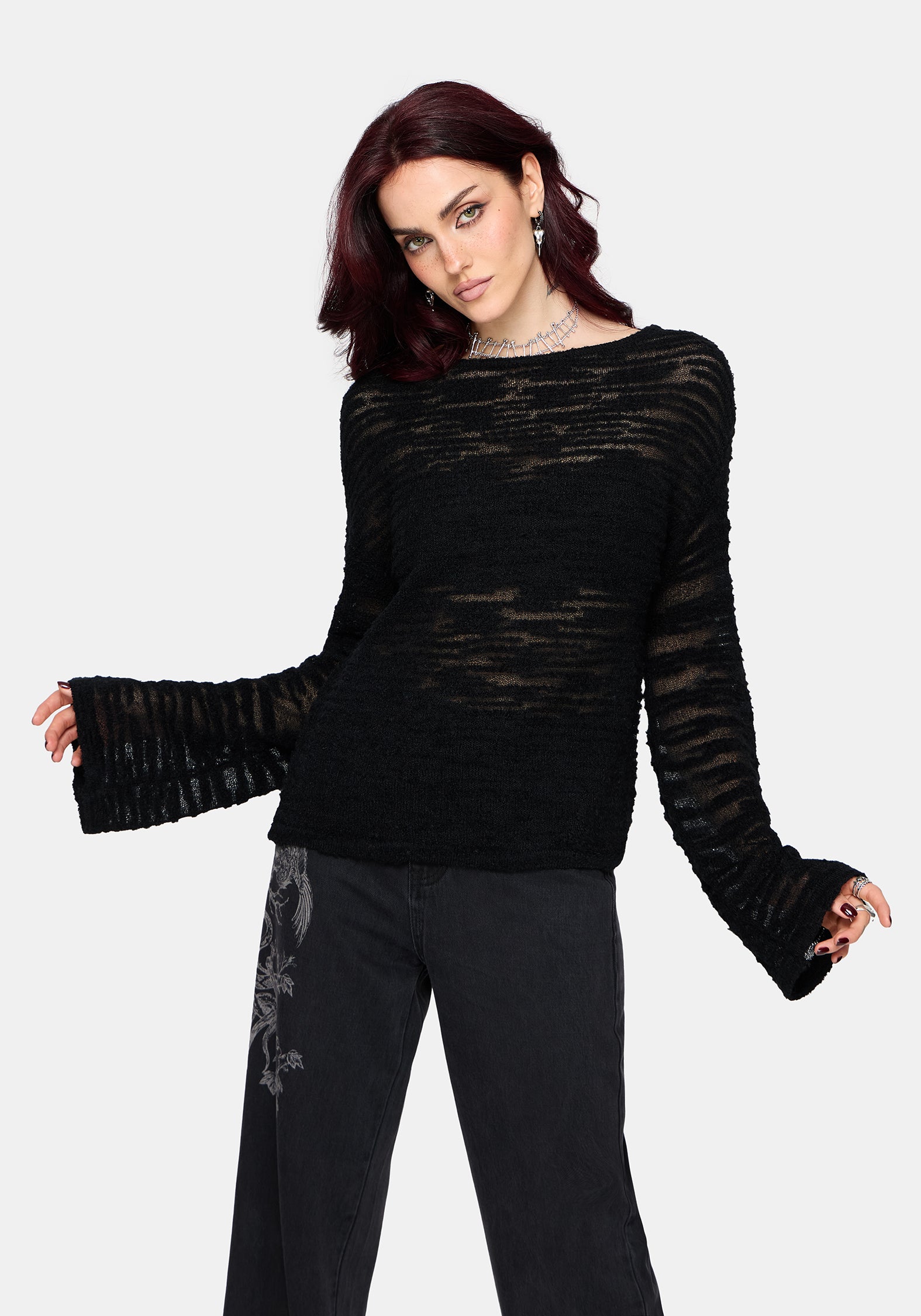 Woman wearing a black distressed jumper with long sleeves and back denim jeans on a white background