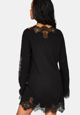 A woman shown from the back wearing a black long-sleeve mini dress with lace trim at the neckline, sleeves, and hem, against a light gray studio background.