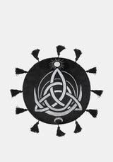 A circular black cushion with a white Celtic knot triquetra design, a small sun motif at the top, and tassels extending from the outer edge, shown on a light gray background.