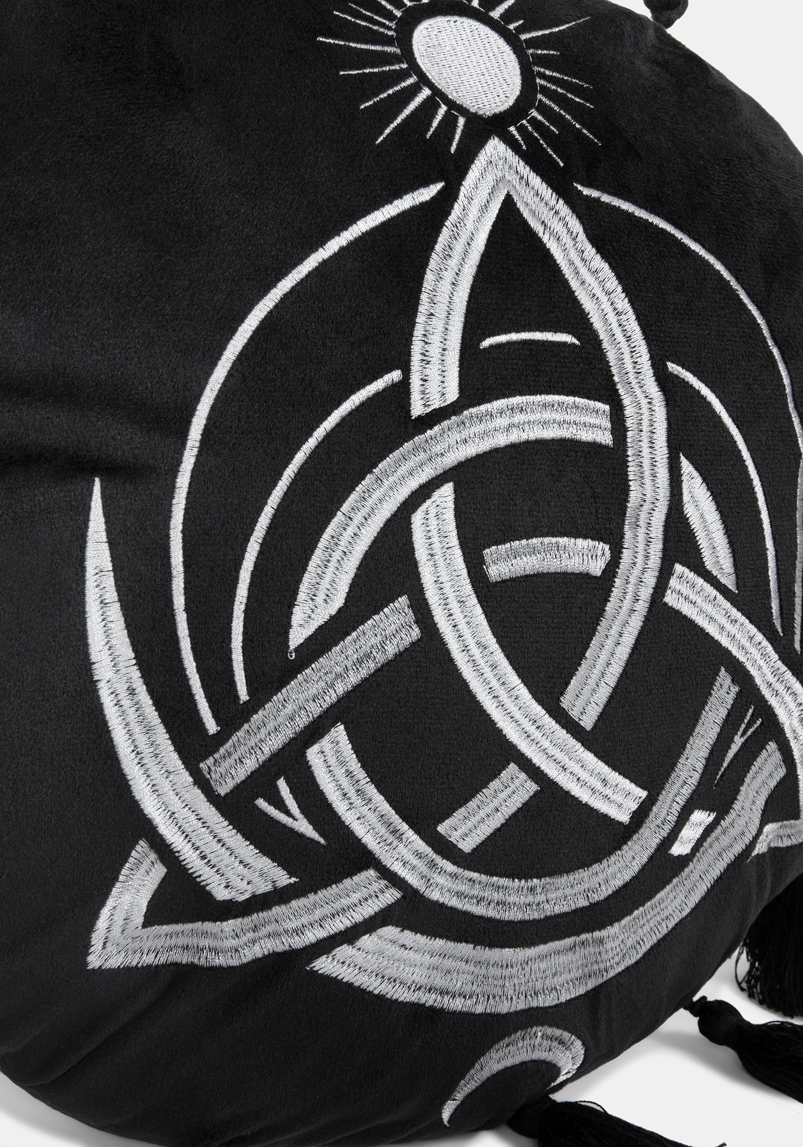A circular black cushion with a white Celtic knot triquetra design, a small sun motif at the top, and tassels extending from the outer edge, shown on a light gray background.