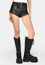 Black faux leather shorts with a front zipper and ruffled waistband, shown on a model wearing black platform knee-high boots against a light gray studio background.