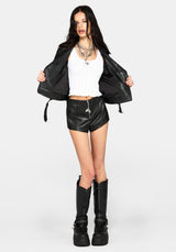 A model wearing a black faux-leather moto jacket, black faux-leather shorts, a white ribbed crop top, and black platform boots, posed against a light gray studio background.