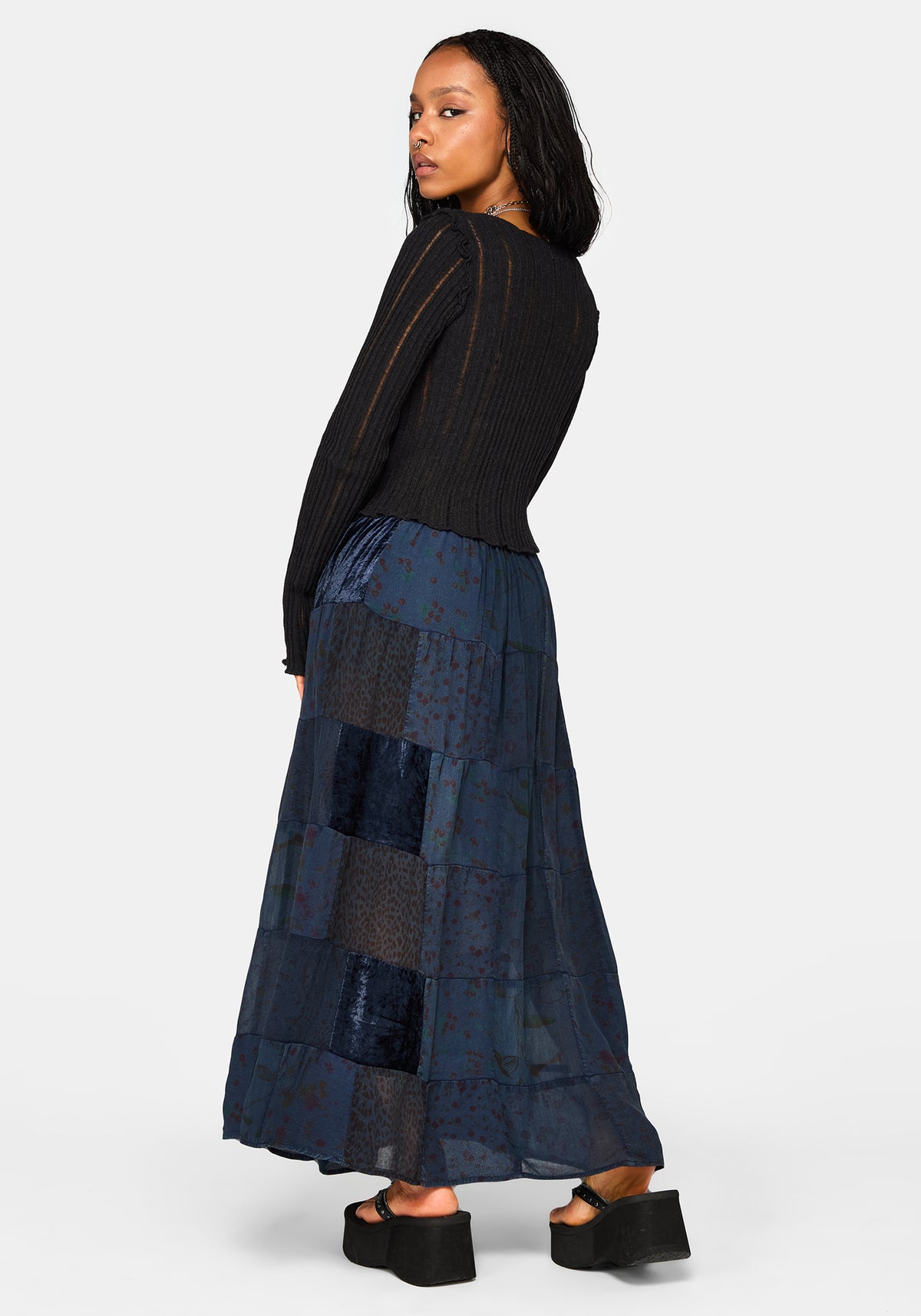 Woman wearing a black top and blue patchwork maxi skirt on a white background