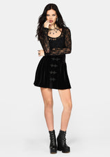 A model wearing a black gothic-style flared velvet mini skirt with bat-wing shaped front buttons, paired with black platform boots, against a light gray background.