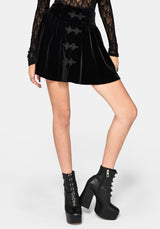 A model wearing a black gothic-style flared velvet mini skirt with bat-wing shaped front buttons, paired with black platform boots, against a light gray background.