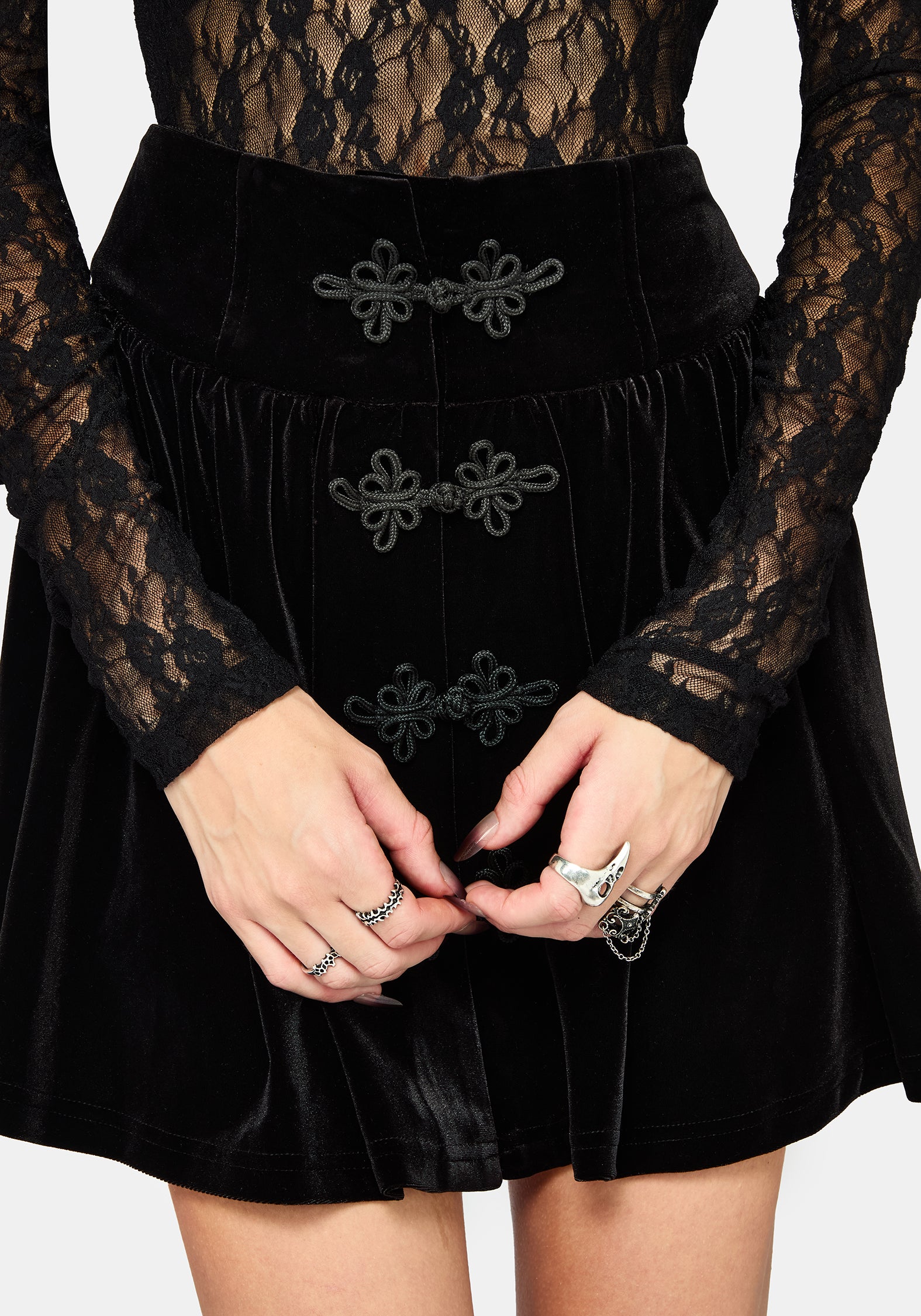 A model wearing a black gothic-style flared velvet mini skirt with bat-wing shaped front buttons, paired with black platform boots, against a light gray background.